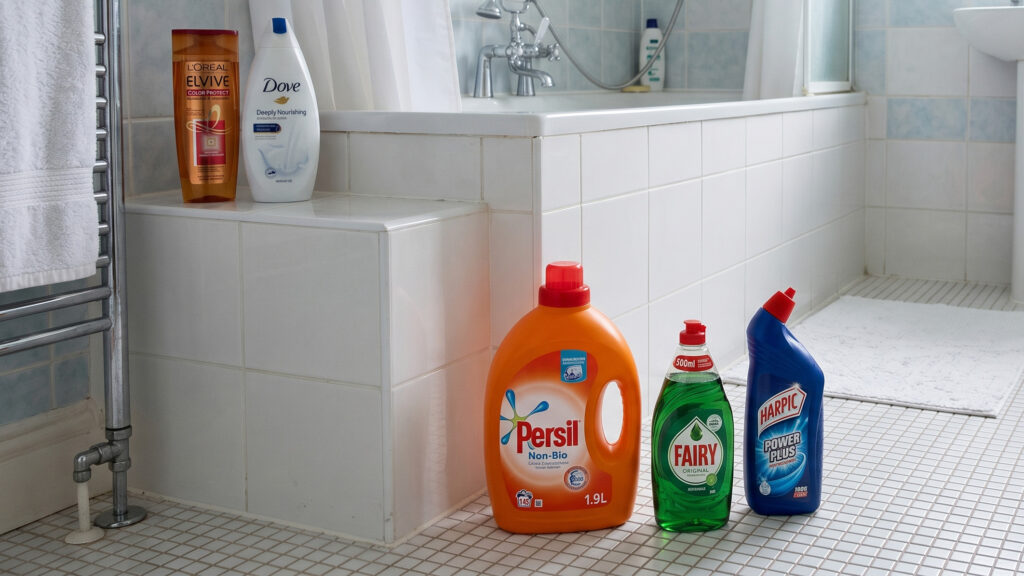 Prodotti per la pulizia domestica e articoli da toeletta esposti in un bagno rivestito di piastrelle.